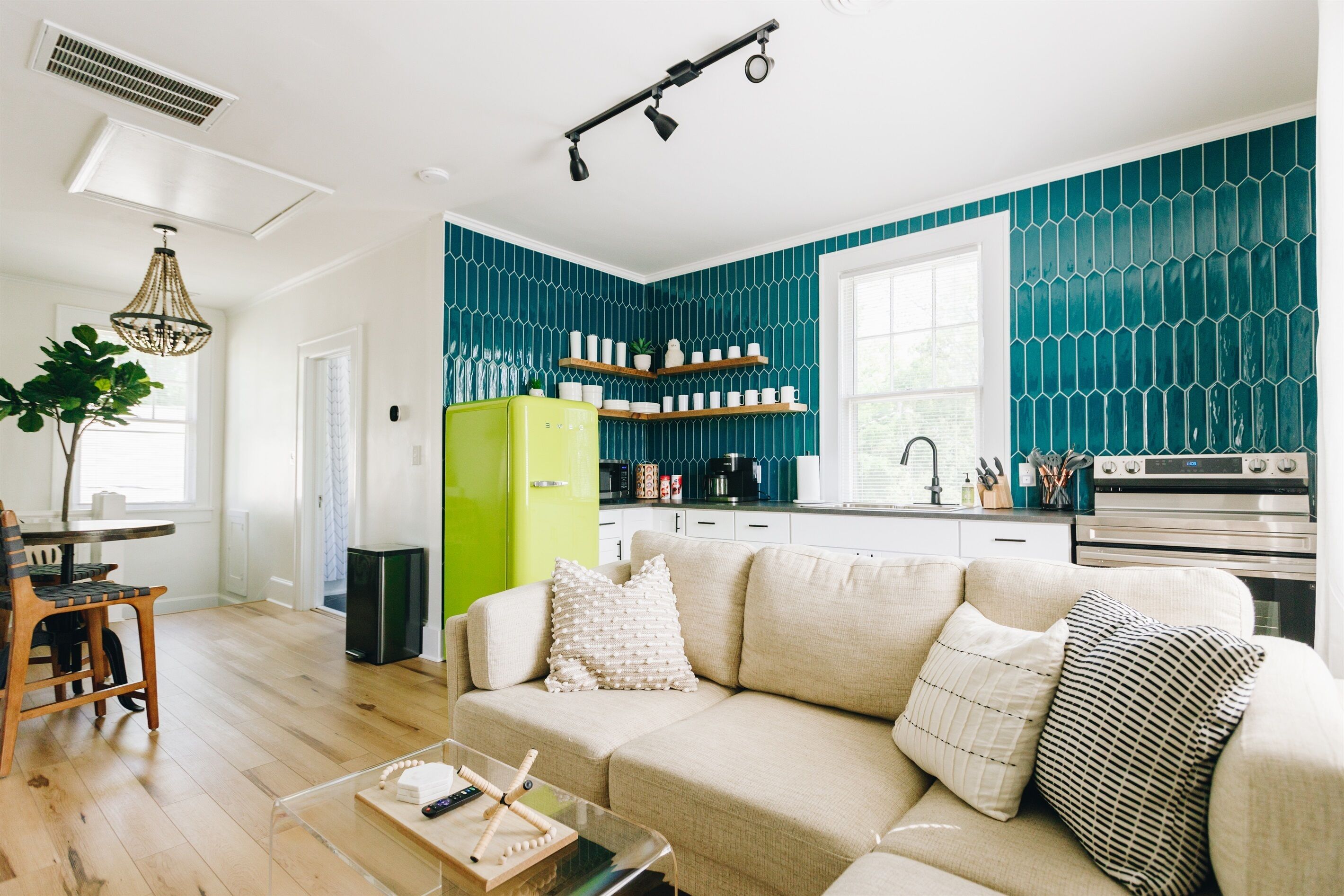 A modern kitchen with teal backsplash, a green refrigerator, and a dining area with a wooden table and chairs.