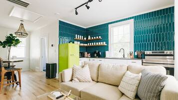 A modern kitchen with teal backsplash, a green refrigerator, and a dining area with a wooden table and chairs.