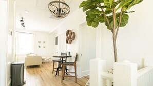 A bright, spacious living area with a wooden floor, a dining table with chairs, a sofa, and a large plant.