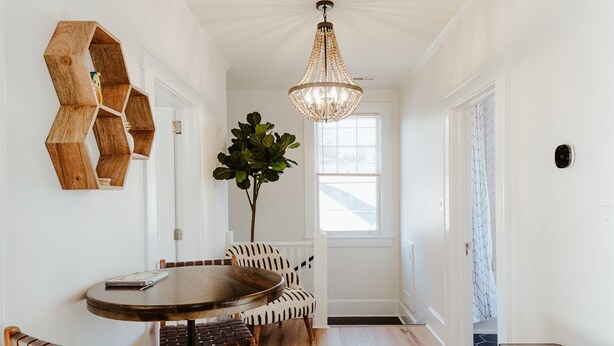 A dining area with a round table, two chairs, a chandelier, a wooden hexagonal shelf, and a potted plant.