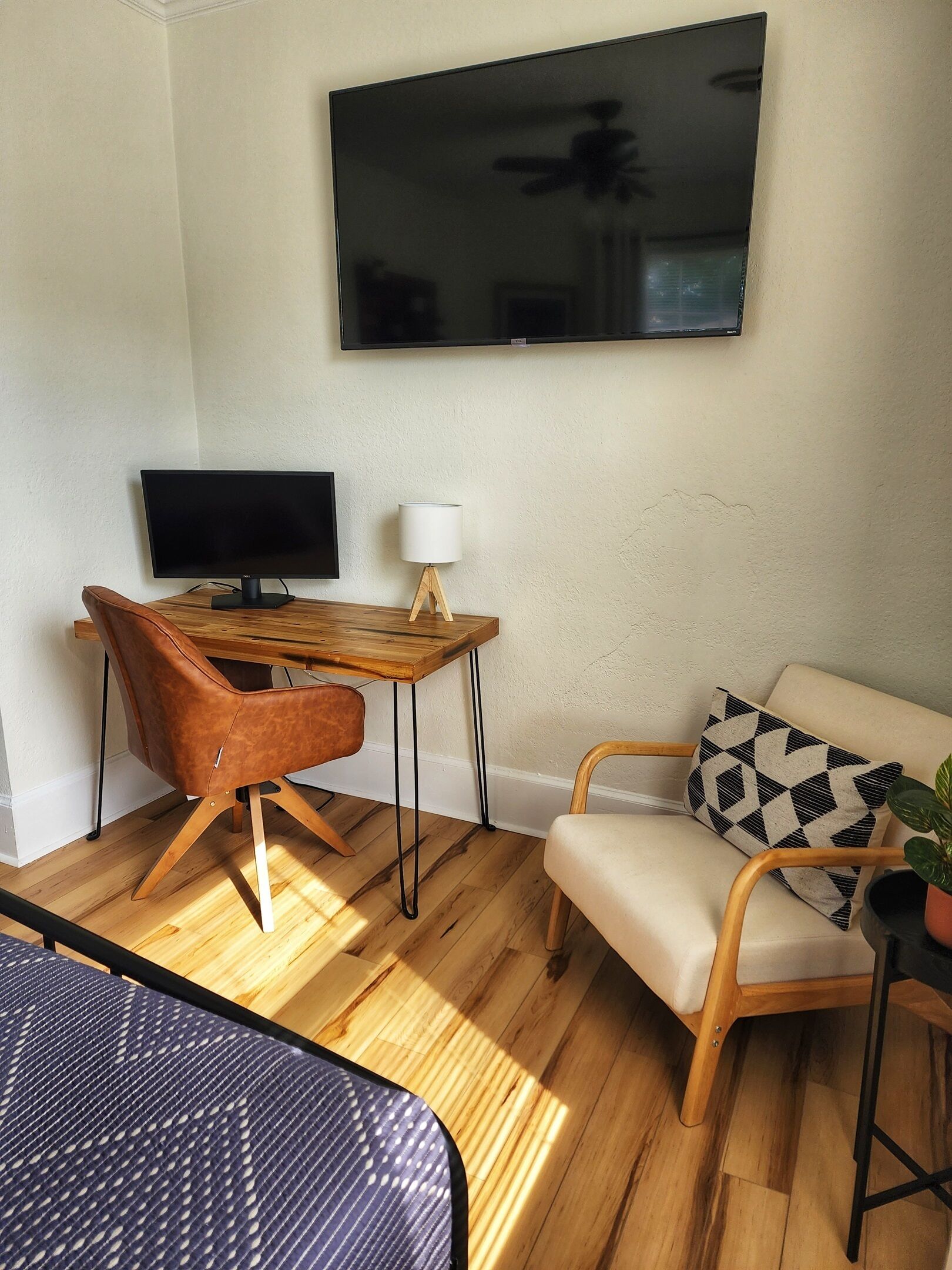 Una sala moderna con una mesa de madera, un sillón de cuero, un sofá con cojines estampados y un televisor de pantalla plana montado en la pared.