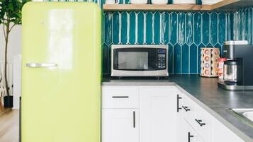 A kitchen with a teal backsplash, a green refrigerator, white cabinets, a microwave, and a coffee maker on the counter.