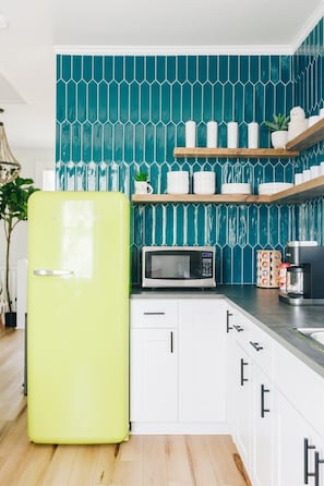 A kitchen with a green refrigerator, white cabinets, a microwave, and a teal backsplash.