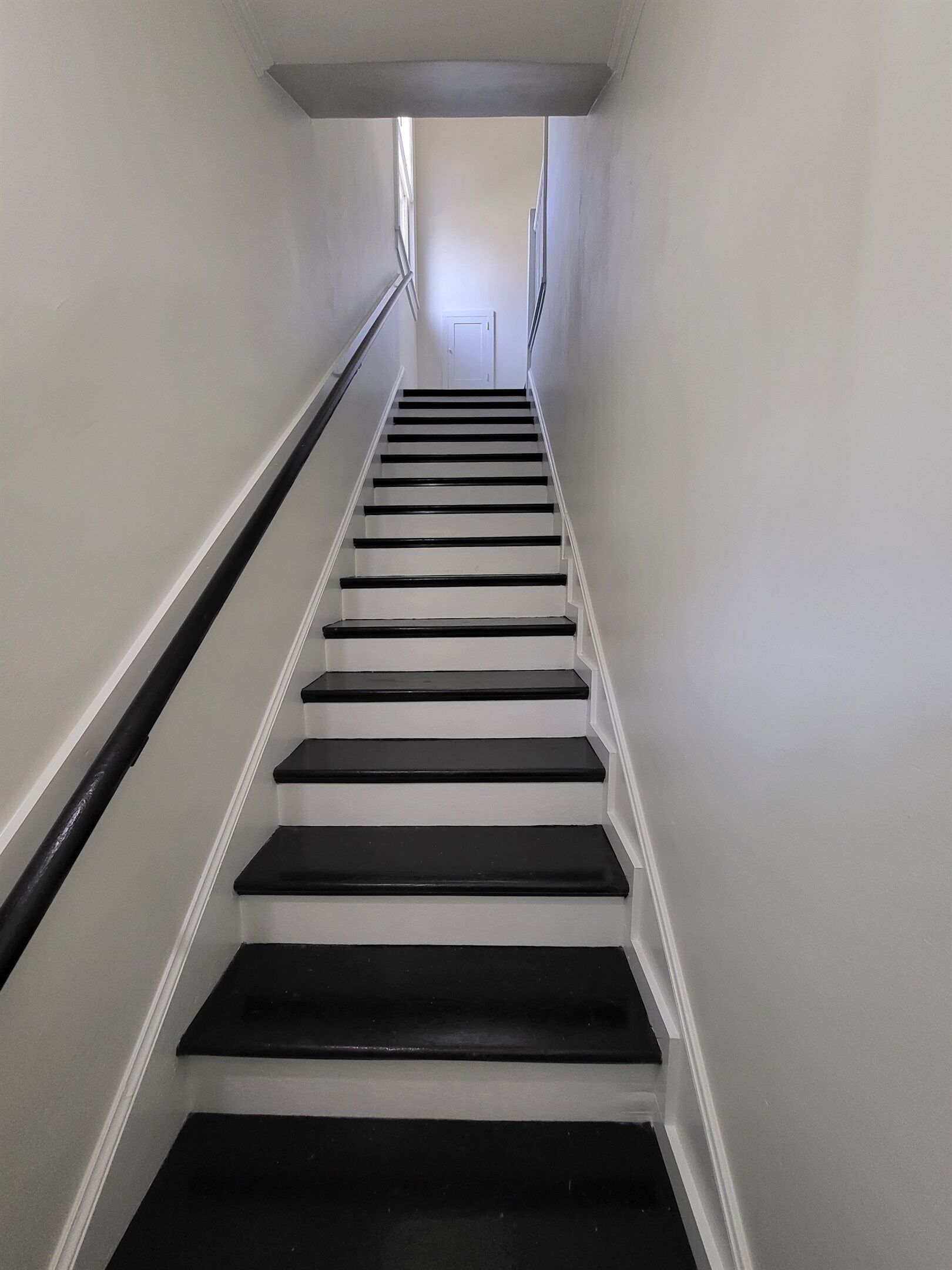 A staircase with black steps and white walls, leading to a door at the top.