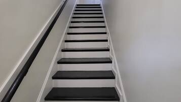 A staircase with black steps and white walls, leading to a door at the top.