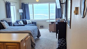 Una habitación con cama, escritorio, silla, ventana con cortinas y vista al océano.