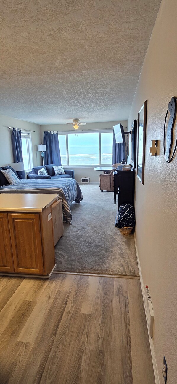 A room with a bed, a desk, a chair, a window with curtains, and a view of the ocean.