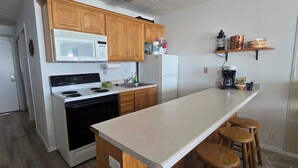 Cocina con gabinetes de madera, microondas, estufa, refrigerador y una barra con taburetes.