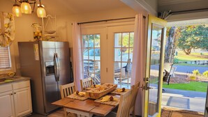 A kitchen with a wooden table, chairs, a refrigerator, and a window with a view of the outside. - 5-Star Lakefront Beach House in Ocean Lakes (Myrtle Beach)