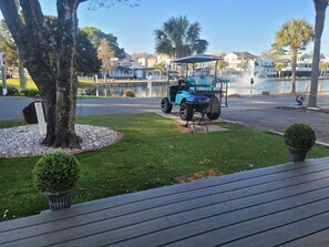 A golf cart parked near a water feature, surrounded by a well-maintained lawn and a wooden deck.