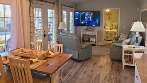 A living room with a television, seating, a dining area, and a view through a glass door. - 5-Star Lakefront Beach House in Ocean Lakes (Myrtle Beach)