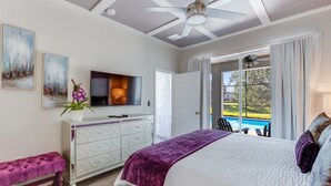 Una camera da letto con un letto grande, una TV, una cassettiera e una panca. Si apre una porta su un balcone con vista sulla piscina.
