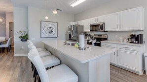 Una cucina moderna con mobili bianchi, elettrodomestici in acciaio inossidabile e un'isola in marmo con sgabelli da bar.