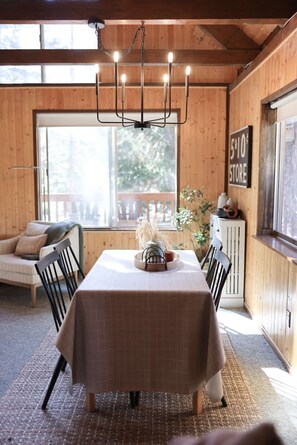 A dining area with a table set for four, a chandelier, and a view of the outdoors through a large window.