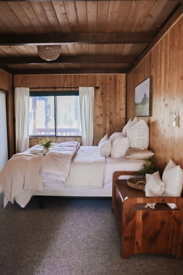 A wooden cabin bedroom with a bed, a wooden bench, and a window with curtains.