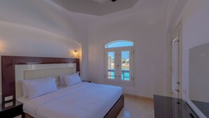 A bedroom with a large bed, a nightstand, a TV, and a window with a view of the beach. - VESTA - Luxury Villa - 5BR - Sabina (Hurghada)