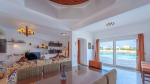 A spacious living area with a large glass door leading to a pool, a chandelier, and a flat-screen TV on a shelf. - VESTA - Luxury Villa - 5BR - Sabina (Hurghada)