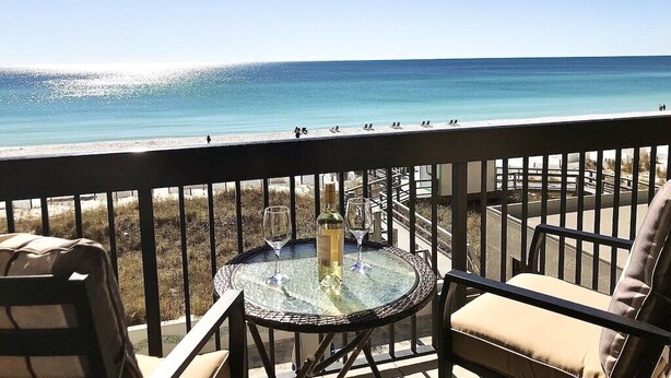 A balcony with a glass table, two chairs, and a bottle of wine.