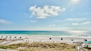 A beach with a clear sky, a sandy shore, and a small building with a green roof.