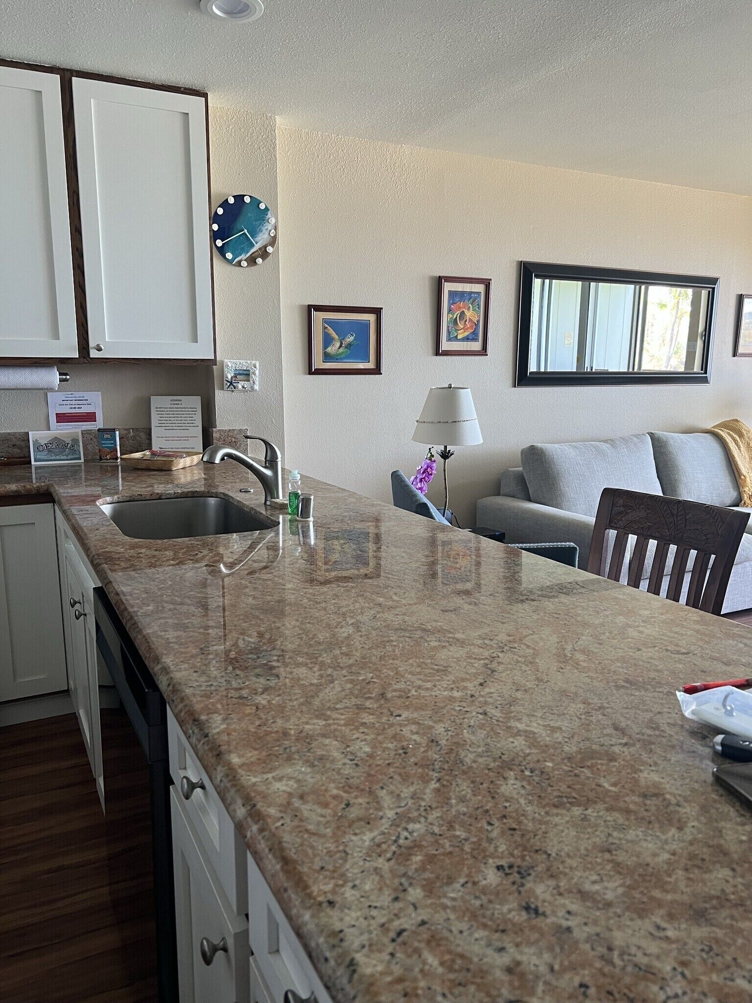 A kitchen with granite countertops, a sink, and a dining area with a table and chairs. There are framed pictures on the wall and a window with a view.