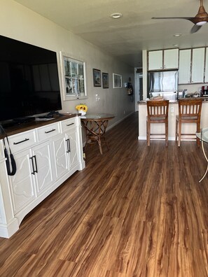 Una cocina moderna con armarios blancos, una mesa de comedor de madera y un televisor.
