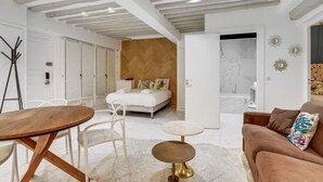 Ein modernes Schlafzimmer mit Holzboden, einem Bett mit weißer Bettwäsche, einem kleinen runden Tisch und einem braunen Sofa.