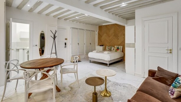 Ein modernes Hotelzimmer mit Holzboden, einem Bett mit Holz Kopfteil, einem weißen Sofa und einem runden Couchtisch.
