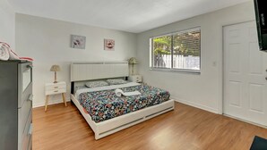 Un dormitorio con cama, mesita de noche, lámpara, cómoda y ventana con persianas.
