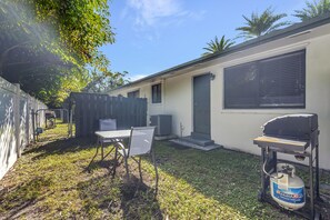 A backyard with a grill, a propane tank, and a table with chairs.