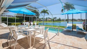 Un espace extérieur abrité comprenant une piscine, des chaises longues et une table dressée pour les repas.