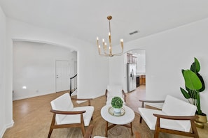 A spacious living room with a chandelier, white furniture, and a potted plant.