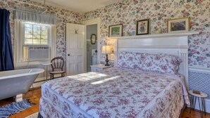Ein Schlafzimmer mit einem großen Bett, einer antiken Badewanne und blumigem Wandpapier.