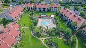Um hotel com piscina central rodeada por espreguiçadeiras e palmeiras.