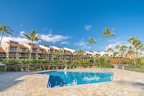 Um hotel com piscina, palmeiras e céu azul claro.
