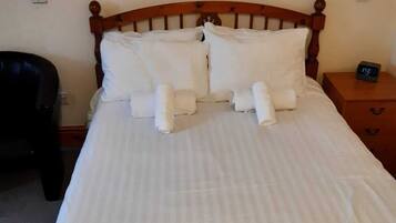 Una cama bien hecha con sábanas y almohadas blancas, un cabecero de madera y una mesita de noche con un reloj digital.