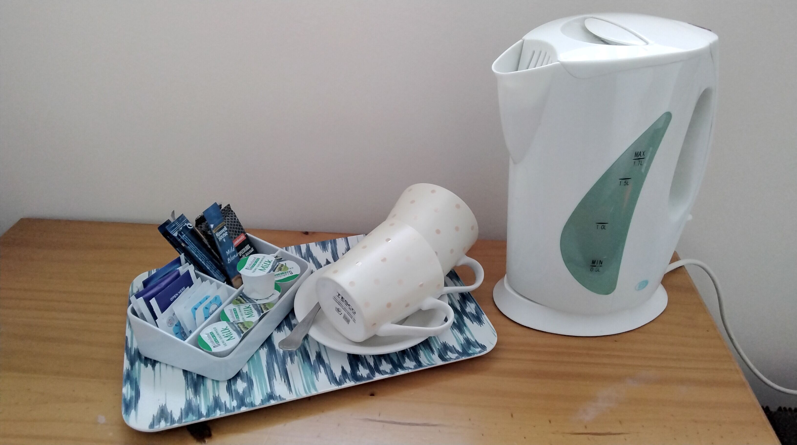 A white electric kettle and a tray with milk cartons and a white mug on a wooden table.