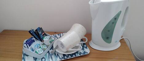 A white electric kettle and a tray with milk cartons and a white mug on a wooden table.