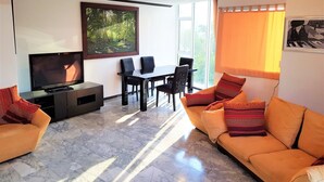 A living room with a TV, sofa, and dining area. - Pratumnak 1 bed With sea View at Siam Oriental Twins (Pattaya)
