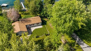 Une maison avec un toit en pente, entourée d’une végétation luxuriante et bordée par un plan d’eau.