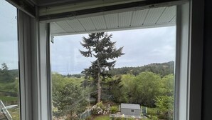 Une pièce dotée d’une grande fenêtre donnant sur un jardin avec des arbres et une petite maison.