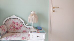 Una habitación con un sofá floral, una mesita de noche blanca con libros y una puerta con tirador de latón.
