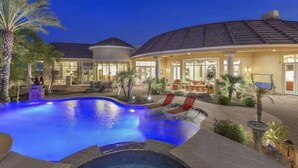 A pool area with lounge chairs, palm trees, and a building with a curved roof.