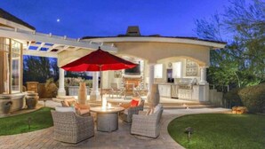 An outdoor patio with wicker furniture, a red umbrella, and a grill area.