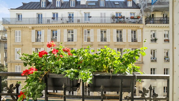 A balcony with a flower planter and a pharmacy sign in the background.