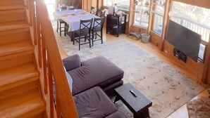 Interior de una cabaña de madera con comedor, sofá y escalera.