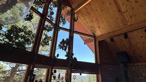 Una habitación con vigas de madera en el techo, ventanas amplias con plantas y una pared de piedra.