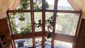 Una cabaña acogedora con techo alto y ventanas grandes. En el interior, hay una mesa de comedor con mantel blanco y un tapete en el suelo.