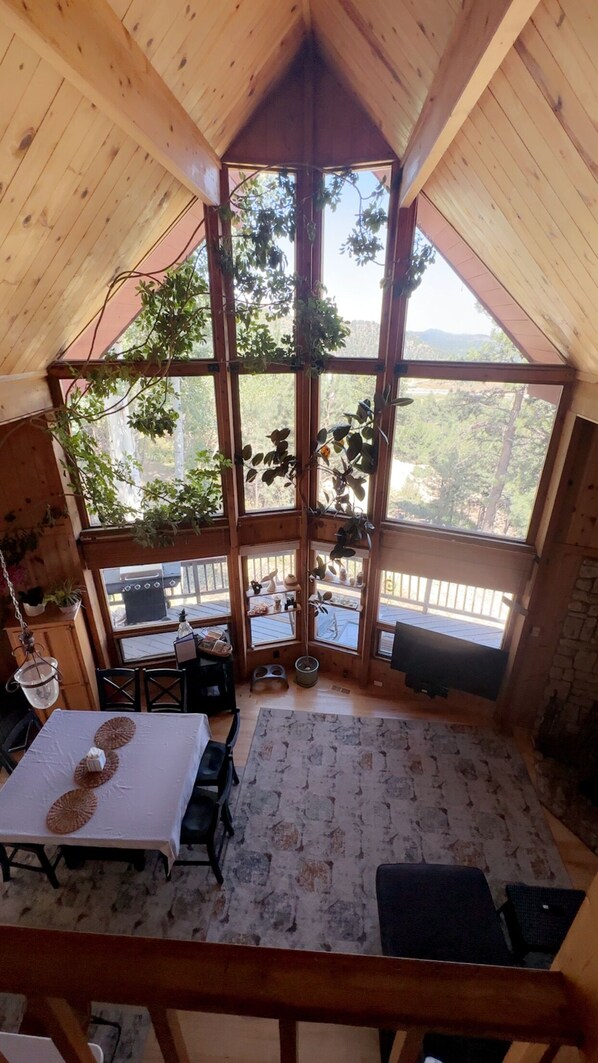 A cozy cabin with a high ceiling and large windows. Inside, there's a dining table with a white tablecloth and a rug on the floor. - Aspen Tree Ranch w Hot Tub Evergreen Colorado (Evergreen)