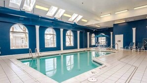 An indoor swimming pool with clear blue water, surrounded by blue walls and large windows.