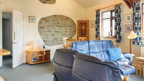 Een woonkamer met een blauwe leren bank, een stenen muur, een houten kast en een raam met gordijnen.
